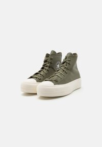 Olive green high-top sneakers with lace-up design, white rubber toe cap and textured outsole, featuring a round logo patch on the side.