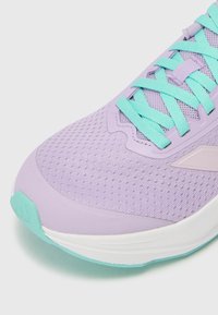 Chaussure de sport lilas clair avec un dessus en maille respirante, des lacets turquoise et une semelle blanche et vert menthe. Contrastes de textures notables.