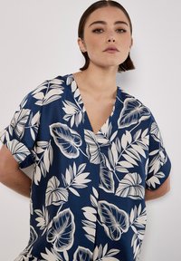 Blusa a maniche corte in navy con motivi a foglia bianchi, caratterizzata da un colletto a V e un tessuto liscio e leggero.