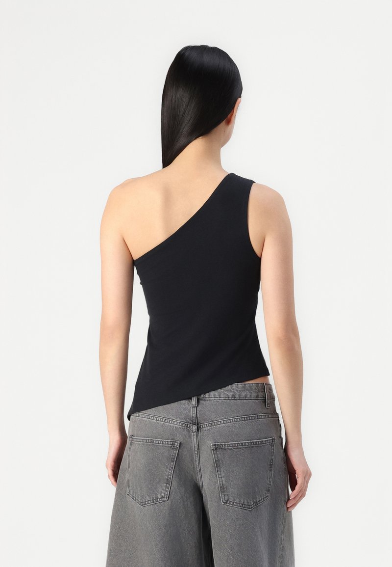 Schwarzes Ein-Schulter-Top aus dehnbarem Material, kombiniert mit hochgeschnittenen grauen Jeans mit Gesäßtaschen und lockerer Passform.