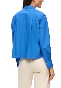 Gekürzte blaue Bluse aus leichtem Stoff, mit Kragen und Knopfdetails an den langen Ärmeln, mit einer glatten Textur.