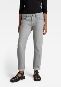 Jean en denim gris à coupe droite, avec un design cinq poches et des ourlets retroussés, associés à des sandales noires à lanières. Look simple et discret.