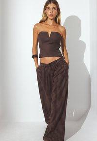 Bruine strapless top met een V-hals ontwerp, gecombineerd met losse, bruine broek met streepjes. Gladde textuur, moderne silhoeët.