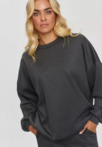 Ciemnoszara, oversize bluza z okrągłym dekoltem i opuszczonymi ramionami, wykonana z miękkiego, teksturowanego materiału; posiada boczne kieszenie.