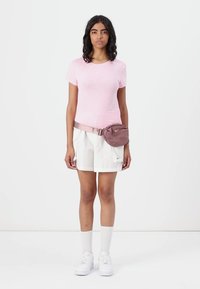 Tricou roz mulat, pantaloni scurți albi cu buzunare laterale și un rucsac fanny. Adidași albi și șosete până la genunchi albe completează ținuta.