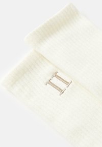 Krämfärgade ribbade strumpor med en mjuk textur, prydda med en liten broderad siffra "II" i beige på sidan.