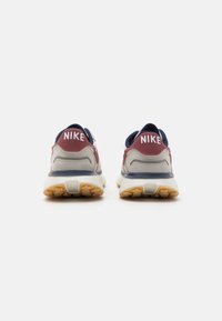 Nike tenisky s měkkým béžovým textilním svrškem, doplněné tmavě modrými a kaštanovými sekcemi. Silná gumová podrážka s texturovaným vzorem.