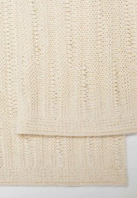 Neulottu kreemivärinen viltti, jossa on teksturoitu kuvio, joka sisältää pystysuuntaisia uria ja vaihtelevia paksuuksia koko kankaan alueella.