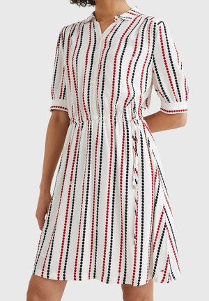 Vestido blanco con rayas verticales de puntos rojos y negros, mangas cortas, cierre de botones en la parte delantera y cintura ajustada con lazo lateral.