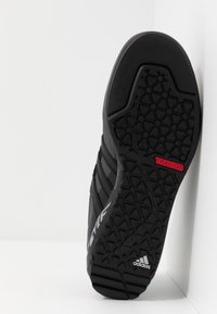 Basket noir avec une semelle en caoutchouc texturé présentant un motif triangulaire. Logos "TRAXION" rouges et "adidas" blancs bien visibles.