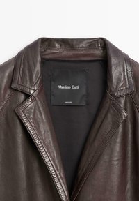 Bruine leren jack met een uitgesneden revers, voorzien van een zwarte binnenlabel met de tekst "Massimo Dutti." Soepele textuur met zichtbare stikseldetails.