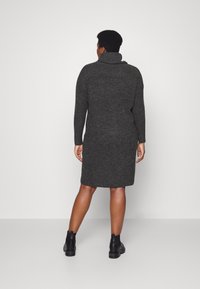 Vestido de malha cinza escuro com decote drapeado, mangas longas e um corte justo, a chegar à metade da panturrilha. Usado com botas pretas até ao tornozelo. Textura suave.