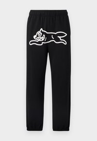 Μαύρο παντελόνι φόρμας με ελαστική μέση, που φέρει μεγάλο λευκό σχέδιο καρτούν ενός πλάσματος που πηδά στο αριστερό πόδι.