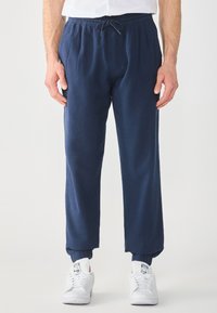Relaxed-fit navy joggers made of lightweight fabric, featuring an elastic waistband with adjustable drawstring and ribbed cuffs.