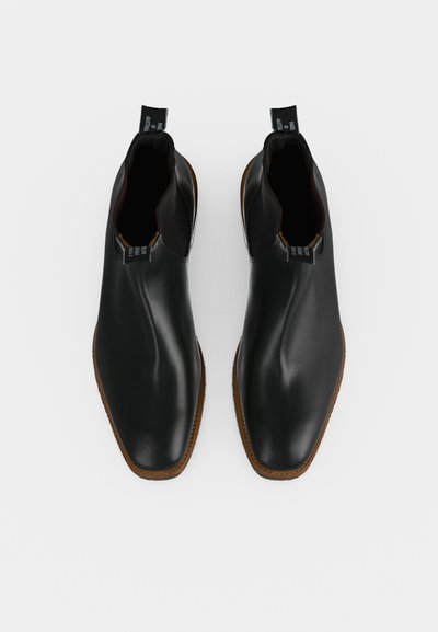 Paire de bottines en cuir noir avec bouts arrondis et semelles marron, vues de dessus sur fond blanc.