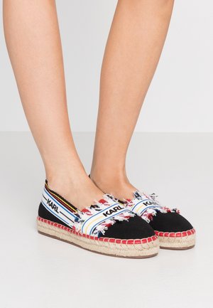 Espadrilles noires avec une semelle épaisse en jute tissé, ornées d'accents effilochés colorés et d'une bride de marque en blanc, jaune et rouge.