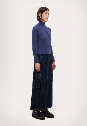 Pulover cu guler înalt, cu dungi violet, asortat cu o fustă lungă din denim închis, cu buzunare laterale. Purtați cu pantofi cu platformă negri.