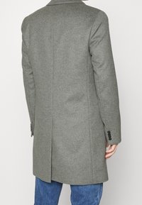 Cappotto grigio in misto lana con taglio dritto, rever a punta e polsini con bottoni, dotato di uno spacco sul retro per facilità di movimento.