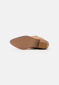 Chaussure beige avec une tige en cuir texturé et une semelle en caoutchouc lisse et solide ; présente un talon modeste et une forme de bout courbée.