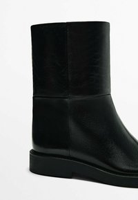 Black leather ankle boot with a smooth texture, straight silhouette, and a flat rubber sole. Features minimal stitching and no visible hardware.