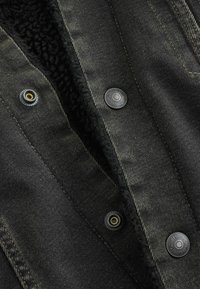 Melns denims jaka ar mīkstu melnu flīsa oderi, ar sudraba pogām un acīmredzamu izturīgu tekstūru.