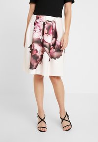 Blommigt mönstrad kjol i krämfärg med rosa och mörklila blommor; plisserad design. Bärs med en svart topp och svarta sandaler med remmar.