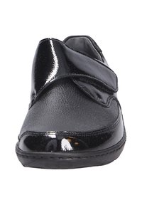 Zwarte schoenen met een gladde, glanzende gepatineerde leren bovenkant, een klittenbandsluiting en een ronde neus. De zool is plat en voorzien van een structuur voor grip.