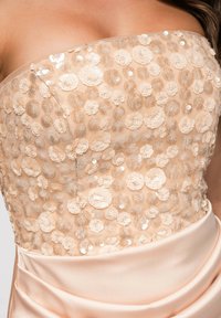 Robe beige bustier avec dentelle florale transparente et ornements en sequins sur le corsage, tissu satin lisse à la taille.