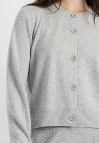 Cardigan grigio chiaro con bottoni realizzato in un tessuto morbido, caratterizzato da un collo rotondo, orlo a coste e quattro bottoni rotondi sul davanti.