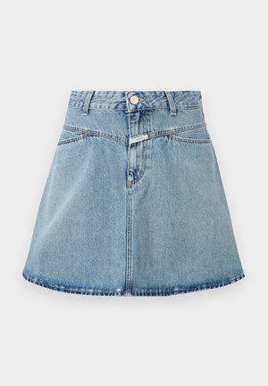 Débardeur marron en maille avec un col en V, associé à une jupe trapèze en denim bleu clair. Les accessoires comprennent un petit sac vert et des chaussures noires.