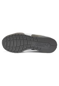 Semelle extérieure en caoutchouc d'une basket Puma avec un motif géométrique de la bande de roulement et un logo embossé près de la zone du talon, présenté sur fond blanc.