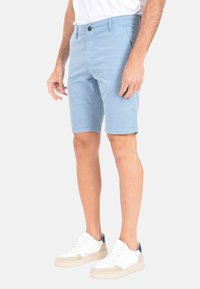 Pantaloni corti azzurro chiaro in cotone con design a vita piatta, cinque tasche e chiusura con bottone, abbinati a sneakers bianche con dettagli in suede.