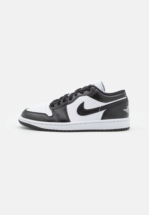 Czarno-biały sneaker Nike Air Jordan 1 Low widoczny z boku, z sznurowadłami, logo Swoosh oraz skrzydlatym emblematem koszykarskim na pięcie.