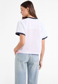 Hvid kortærmet bluse med marineblå kant, der har mesh-detalje på ryggen. Parret med lyseblå afslappede jeans, der viser et casual design.