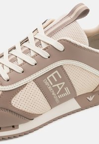 Béžové a taupe tenisky Emporio Armani s bílými tkaničkami, síťovinou a gumovou podrážkou, na které je logo značky na boku.
