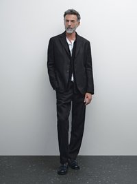Schwarzes Leinenanzug mit einem einreihigen Jackett und maßgeschneiderter Hose, kombiniert mit einem weißen Hemd und schwarzen Schuhen. Glatte Textur und moderner Schnitt.
