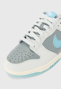 Sneaker Nike in pelle grigio chiaro e bianca, con punta perforata e dettagli turchesi. Caratterizzato da lacci piatti e suola in gomma con dettagli azzurri.