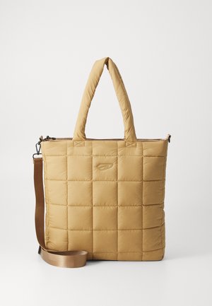 Sac cabas matelassé carré beige avec poignées rembourrées et sangle d'épaule marron réglable sur fond uni.
