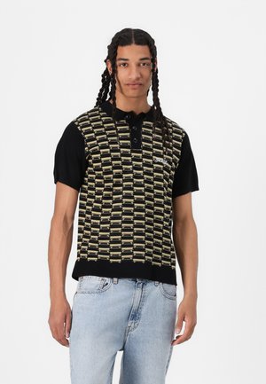 Black and gold patterned short-sleeve polo shirt with a collar, featuring three buttons and a logo, paired with light blue jeans.
