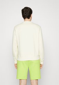 Sudadera color crema con cuello redondo, puños y dobladillo acanalados, combinada con pantalones cortos verdes brillantes que tienen un bolsillo trasero.