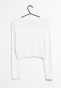 Vitt kortärmat långärmat tröja på en svart galge, tillverkad av lätt och slät tyg. Har en enkel rund halsringning och åtsittande manschetter.