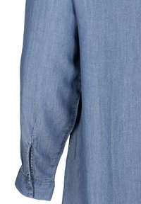 Chemise en denim bleu clair avec des manches longues et un poignet boutonné, au style décontracté. La texture du tissu semble lisse avec des variations subtiles.