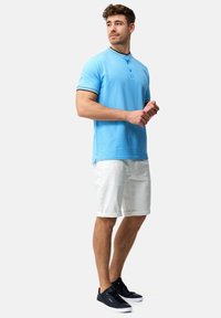Polo de culoare albastru deschis, cu închidere cu butoane și guler cu dungi, asortat cu pantaloni scurți albi și adidași bleumarin, punând în evidență stilul casual de vară.
