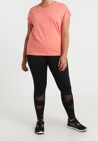 Lys rosa trænings t-shirt med rund hals, parret med sorte leggings med netudskæringer og sorte træningssko.
