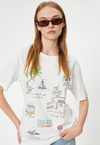 Hvid bomulds t-shirt med farverige trykte designs, herunder palmer, en sejlbåd, et hotelskilt og sætninger som "Endless Summer."