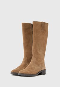 Beżowe zamszowe kozaki sięgające kolan, o gładkiej fakturze, zaokrąglonym nosku i niskim obcasie typu blok. Posiadają boczny zamek błyskawiczny oraz małą pętlę u góry.