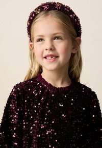 Bordeauxfarbener Pailletten-Top mit einem gerafften Ausschnitt, der eine glänzende Textur aufweist, sowie einem passenden Perlen-Haarband mit floralen Akzenten.