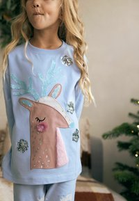 Light blue sweatshirt with a large pink reindeer face design, embellished with sequins and fuzzy textures, paired with matching light blue pants.
