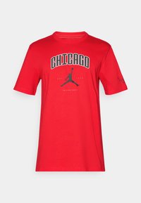 Červené bavlněné tričko s krátkými rukávy, s nápisem "CHICAGO" tučným černým písmem a logem Jumpman uprostřed. Hladký povrch.
