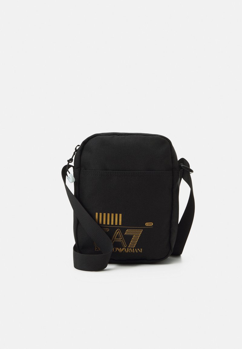 Black crossbody bag made of fabric, featuring a rectangular shape, adjustable strap, and bold gold logo with horizontal stripes.